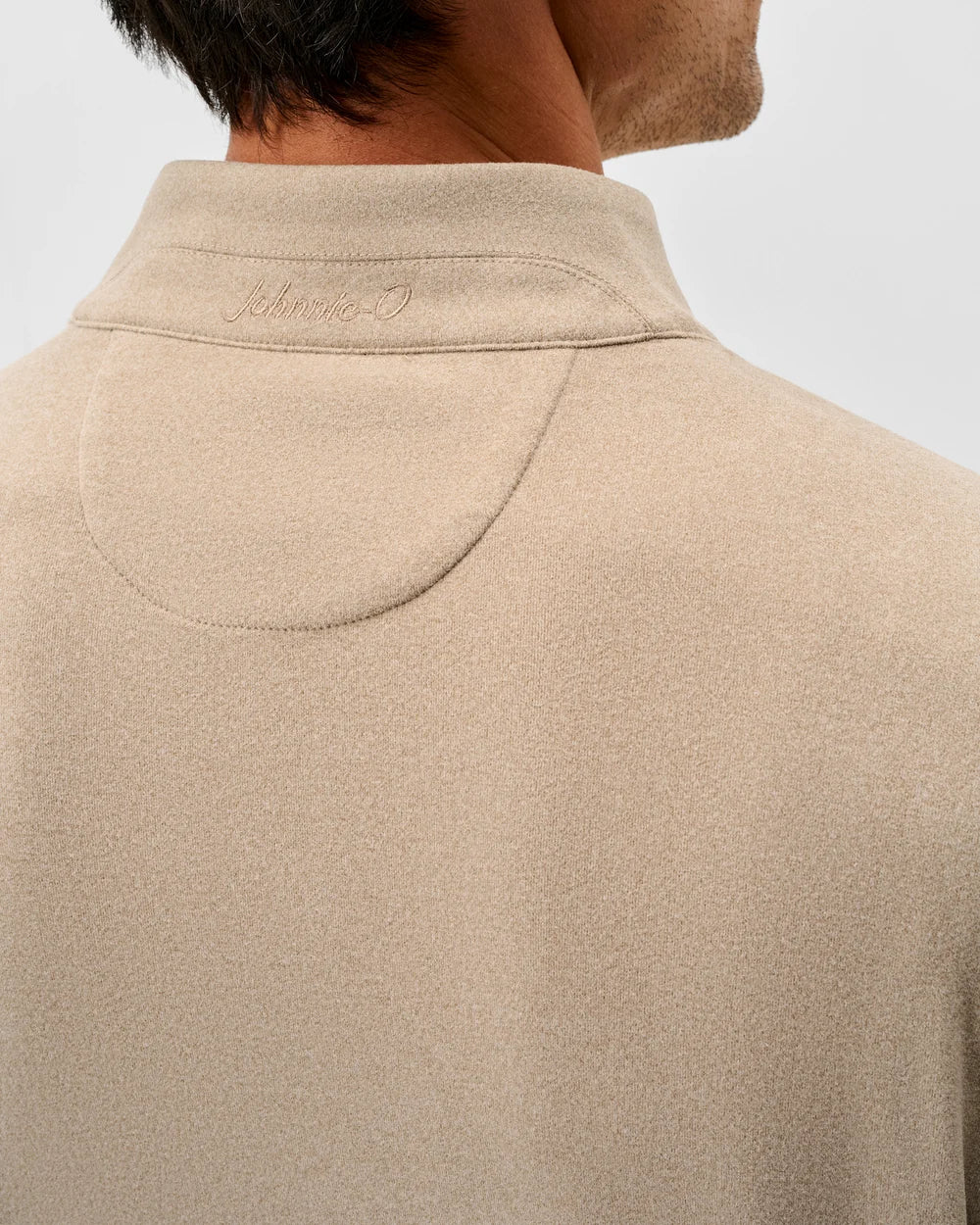 Close-up back view of a man wearing a beige knit polo shirt with a collar and a small embroidered logo on the inside of the neck.