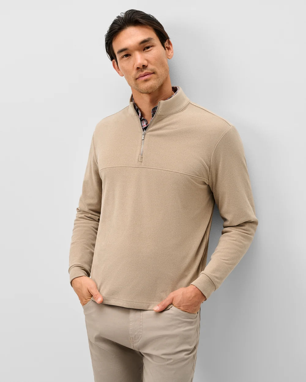 A man wearing a beige quarter-zip long-sleeve pullover sweater and matching beige pants, standing against a light gray studio background.