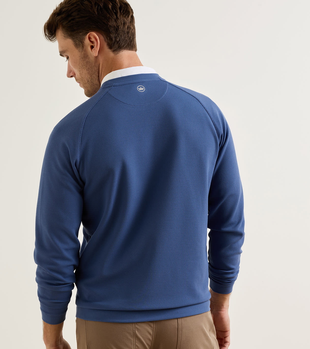 A man wearing a royal blue long-sleeve crewneck sweater, shown from the back against a plain light gray studio background.