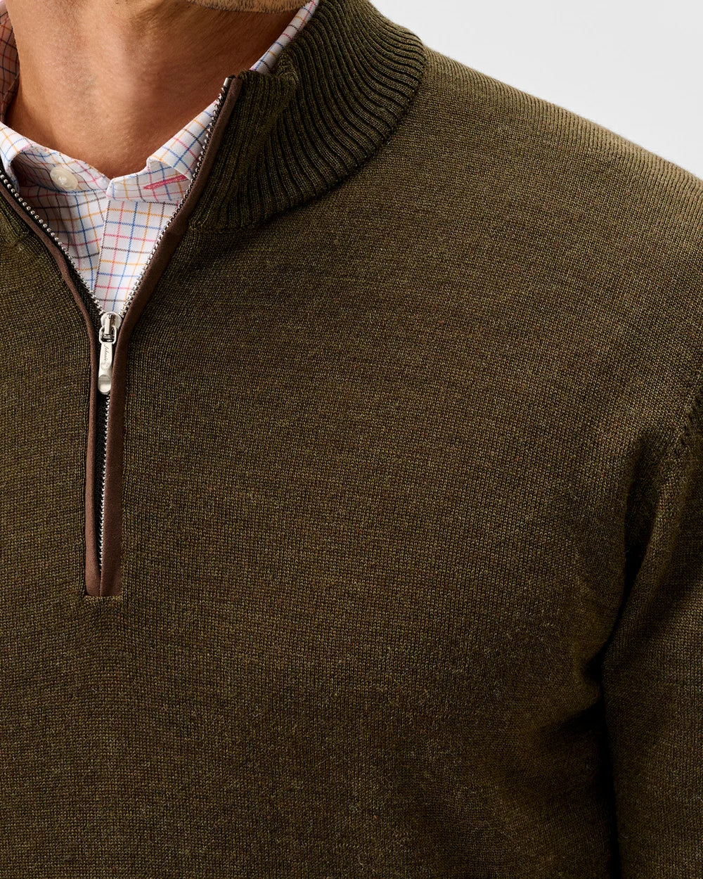 Close-up of a man wearing an olive green ribbed knit quarter-zip sweater over a light plaid collared shirt.