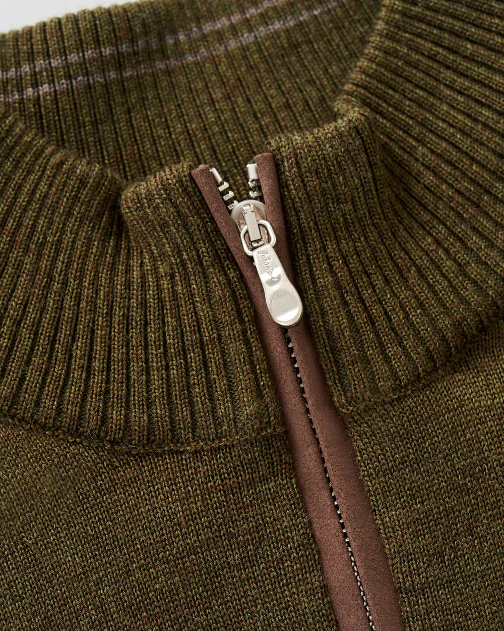 Close-up of a ribbed knit quarter-zip sweater in olive green, showing a brown zipper track and a silver metal zipper pull.
