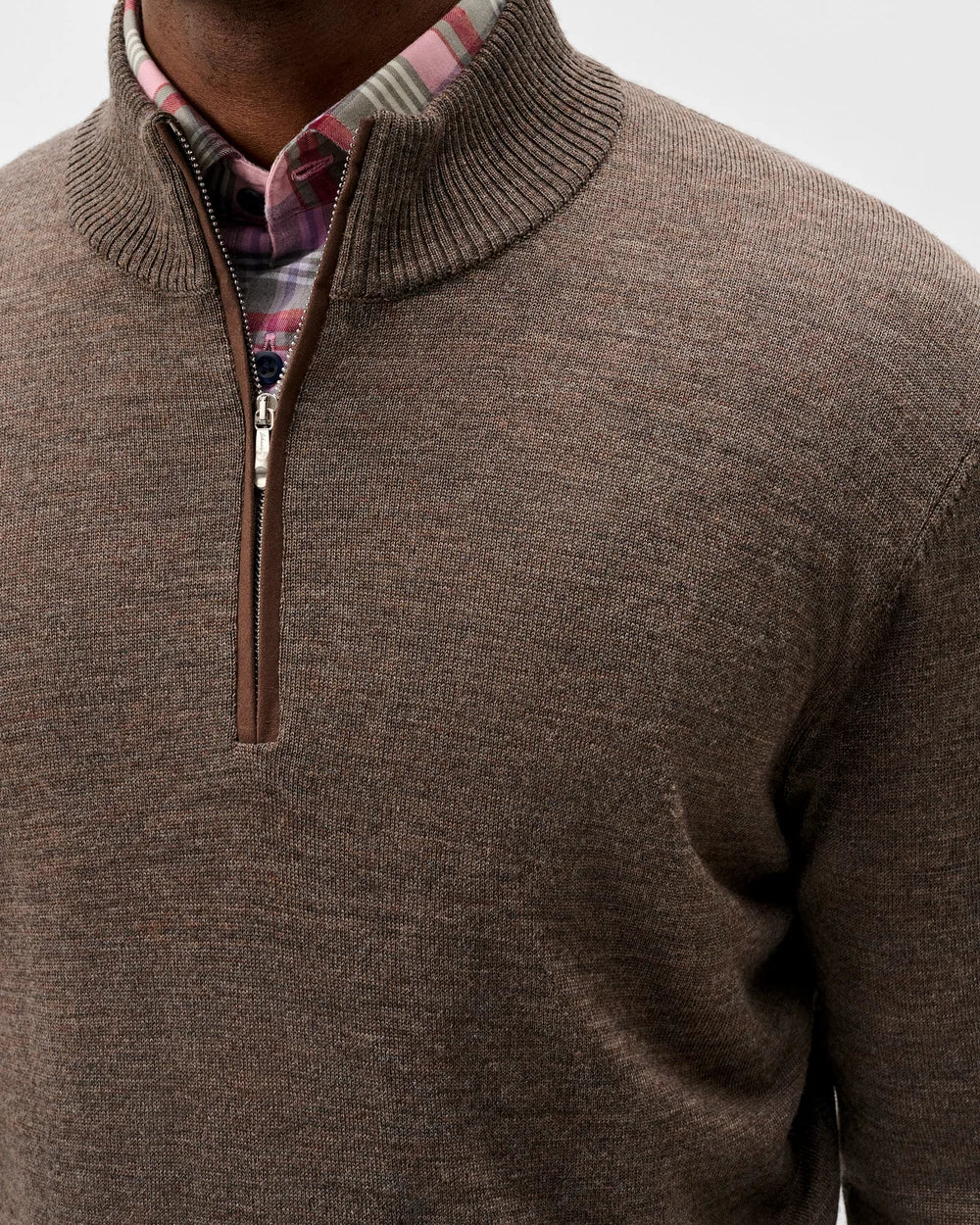 Close-up of a man wearing a brown ribbed knit quarter-zip sweater over a plaid collared shirt.