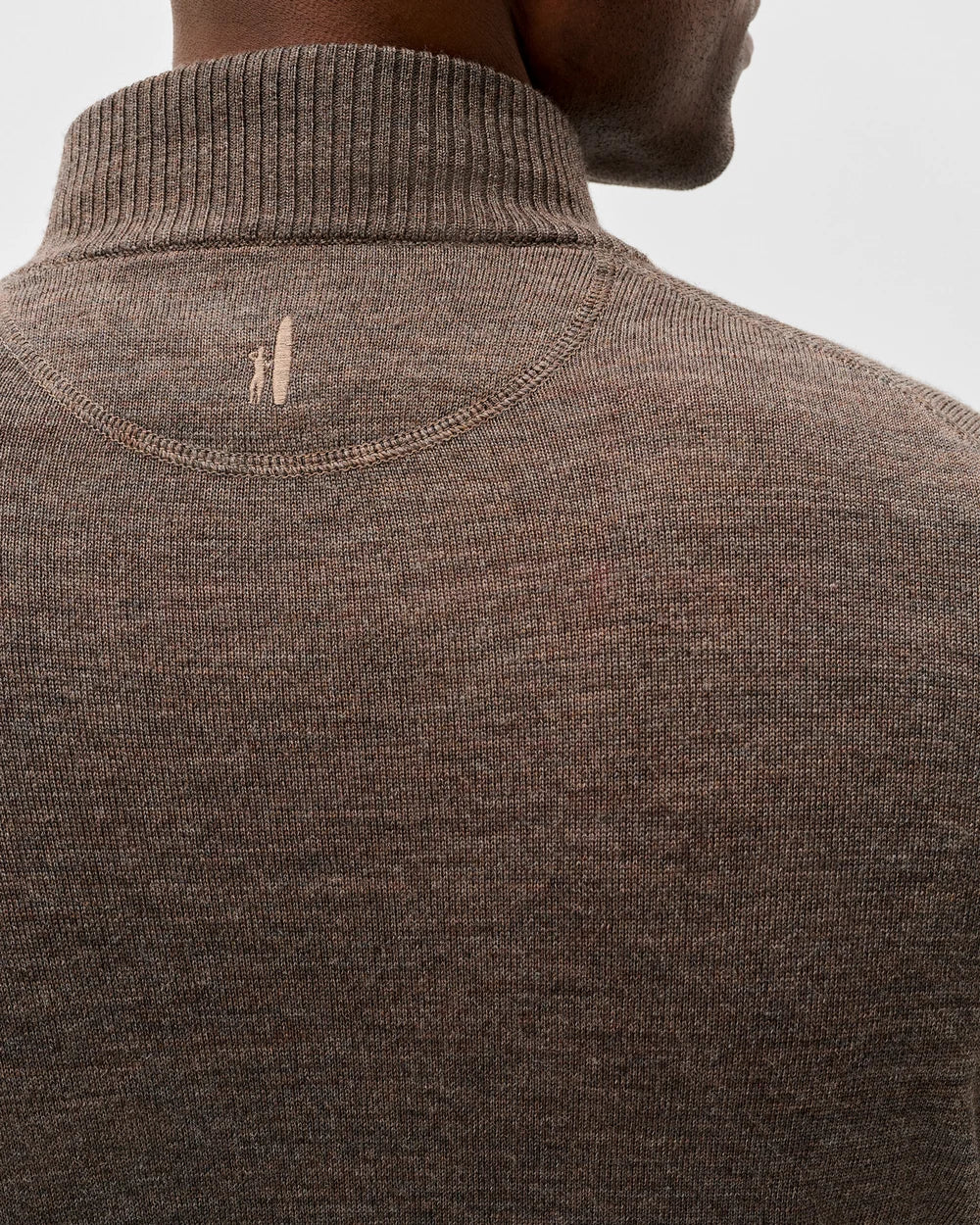 Close-up back view of a man wearing a brown ribbed knit turtleneck sweater, showing a small embroidered logo near the upper neck.