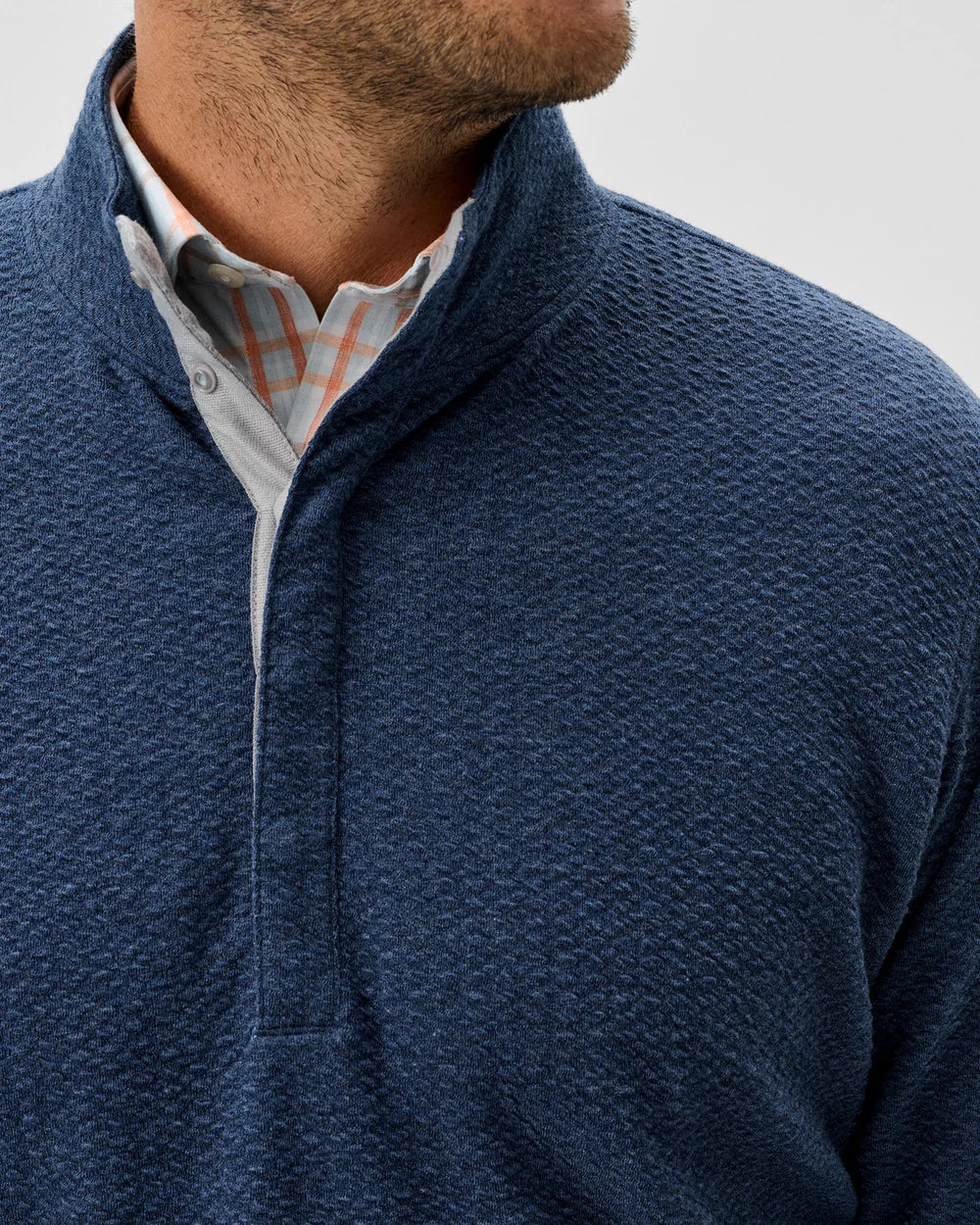 Man wearing a blue textured sweater over a checkered shirt on a light gray background