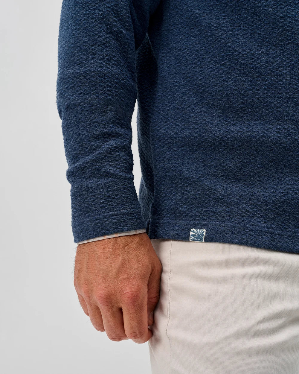 Close-up of a man wearing a blue long-sleeve shirt with a Johnnie-O brand logo on a light gray background