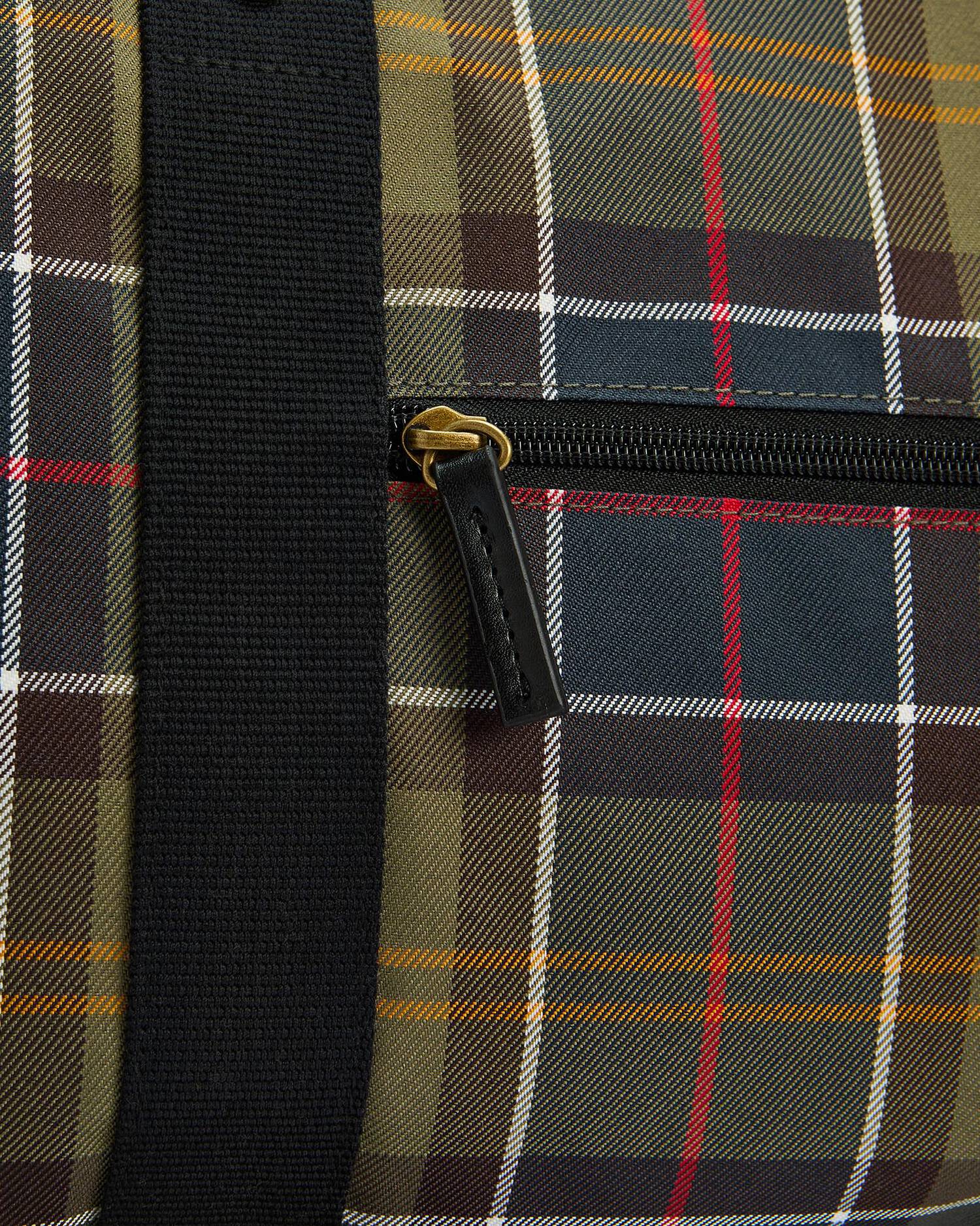 Close-up of a plaid duffel bag with a black webbing strap and a black zipper featuring a gold pull tab.