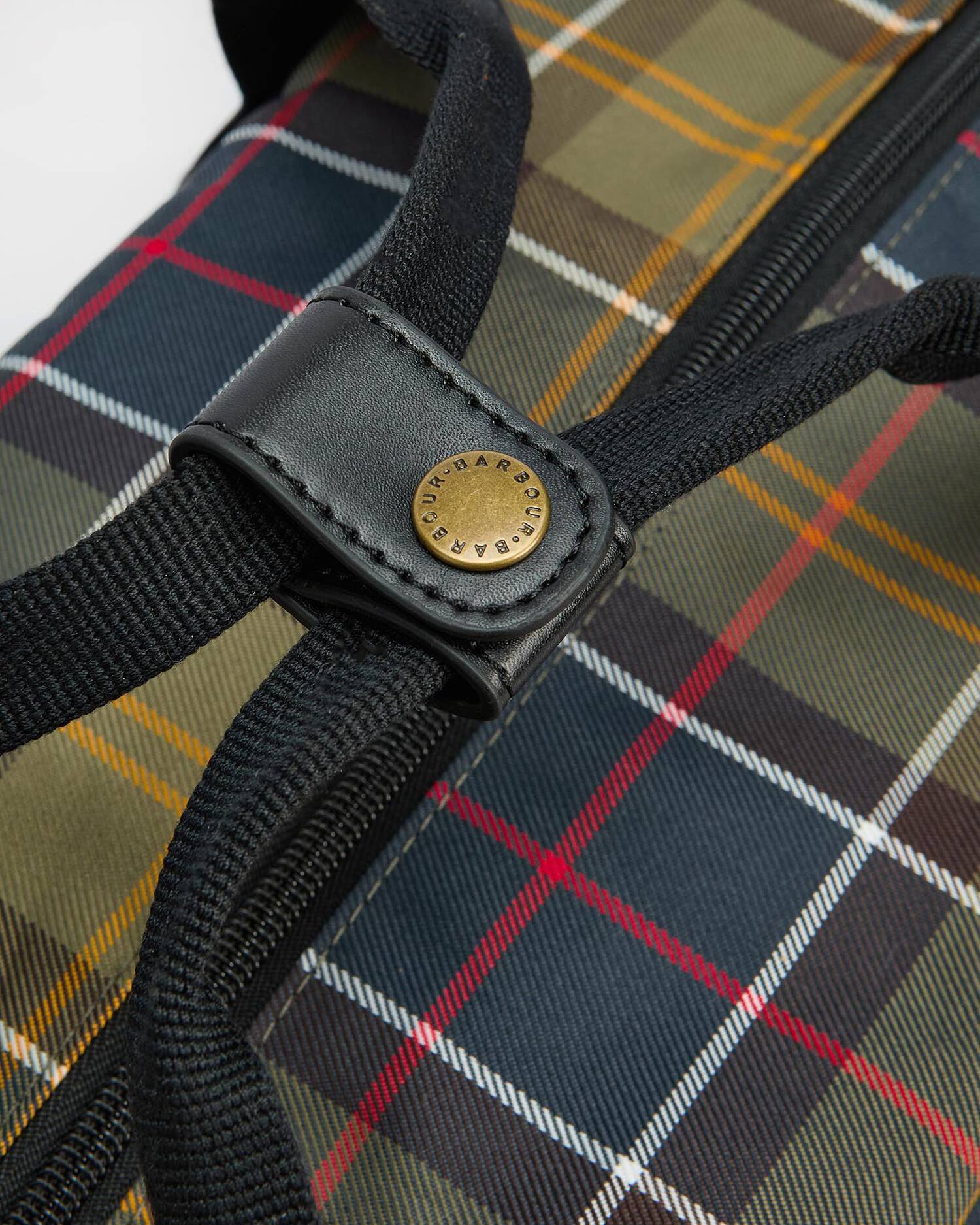 Close-up of a Barbour bag featuring a classic tartan plaid pattern in navy, green, yellow, and red, with a black leather strap and a gold-tone metal brand badge.