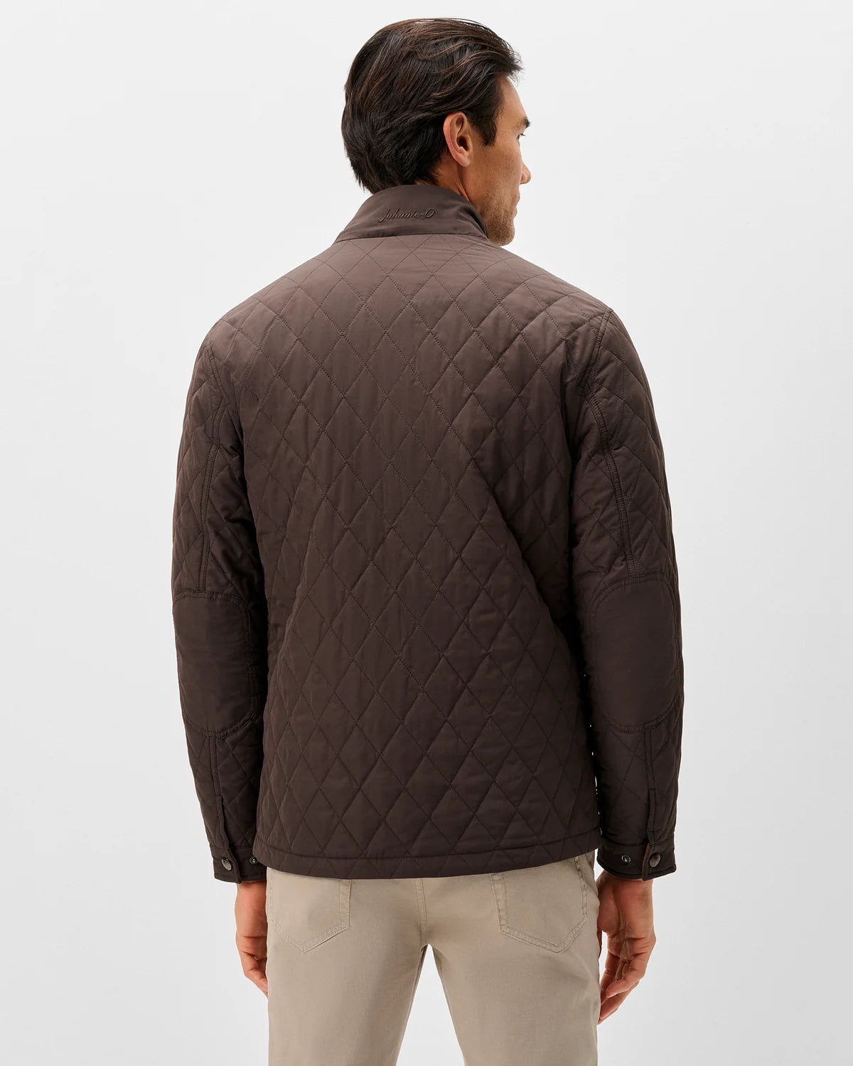 A man shown from the back wearing a dark brown diamond-quilted jacket and light beige trousers, photographed against a clean light gray studio background.