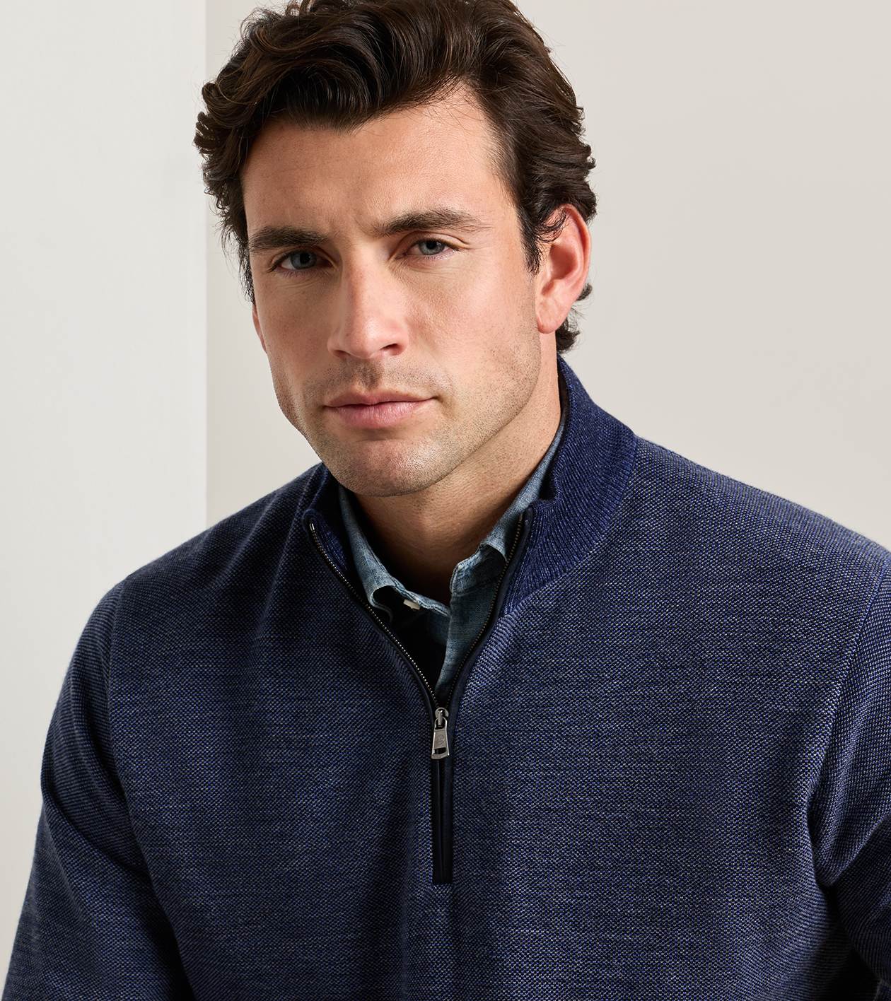 A man wearing a navy blue textured quarter-zip pullover sweater over a collared blue shirt, photographed against a plain light background.