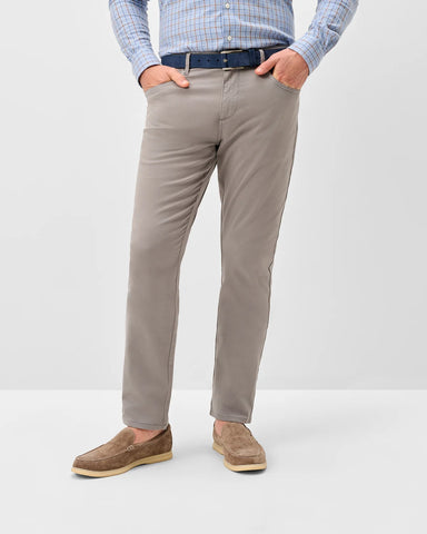 A person wearing slim-fit taupe/beige chinos with a blue belt, a light blue and white checkered shirt, and brown suede loafers, standing against a light gray studio background.