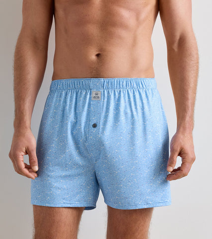 A man wearing light blue boxer briefs with a subtle speckled pattern and a small front button, shown from the chest down against a plain light gray studio background.