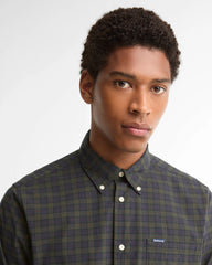 A man wearing a dark green and black plaid button-down shirt by Barbour, photographed against a clean light gray background.