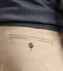 Close-up of the back waistband of beige trousers, showing a buttoned welt pocket and a dark heather gray ribbed knit top folded over the hem.