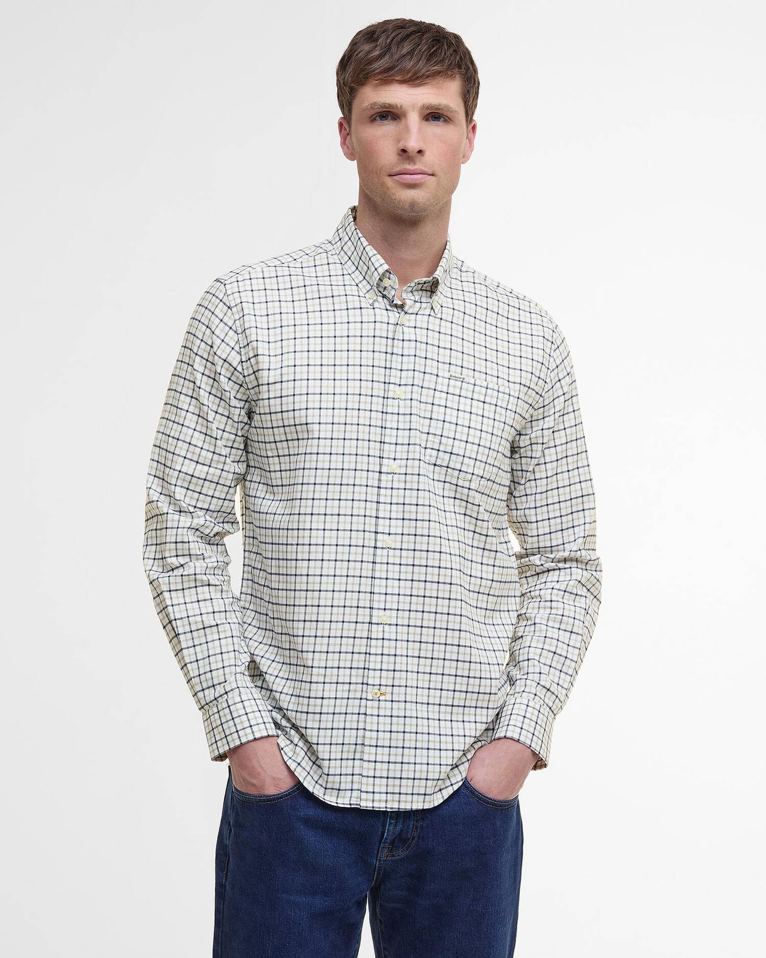 A man wearing a long-sleeve button-down shirt with a white, black, and light blue grid pattern, paired with dark blue jeans, standing against a plain white studio background.