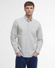 A man wearing a long-sleeve button-down shirt with a white, black, and light blue grid pattern, paired with dark blue jeans, standing against a plain white studio background.