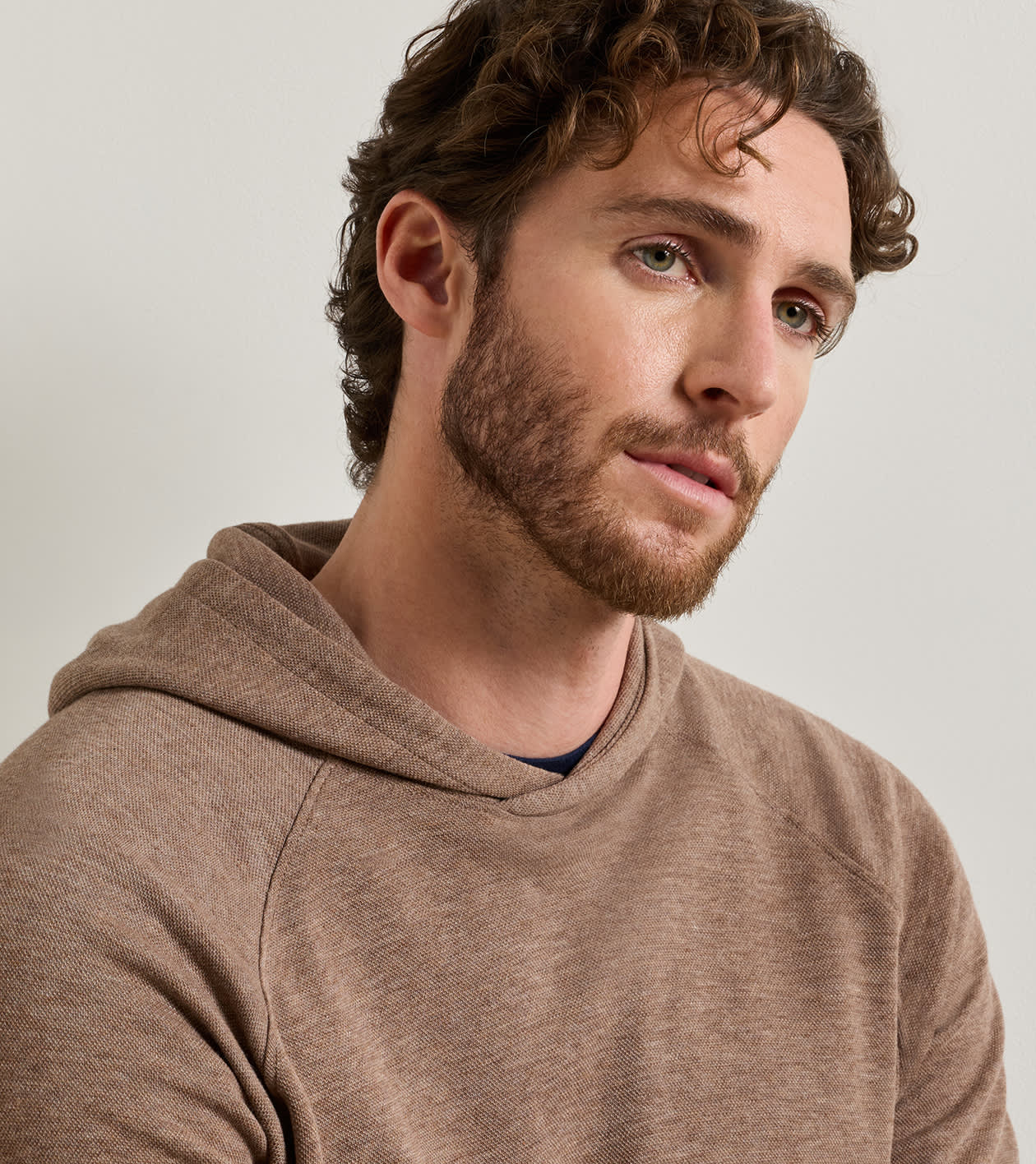 A close-up shot of a man wearing a heathered brown pullover hoodie against a light gray background.
