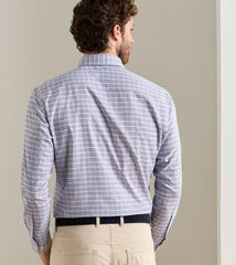 A man viewed from behind wearing a long-sleeve button-down shirt with a fine blue, red, and white plaid pattern, paired with khaki pants and a black belt.