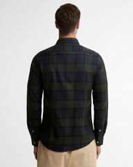 A man viewed from the back wearing a dark green and navy plaid long-sleeve button-up shirt, paired with beige trousers, against a plain white studio background.