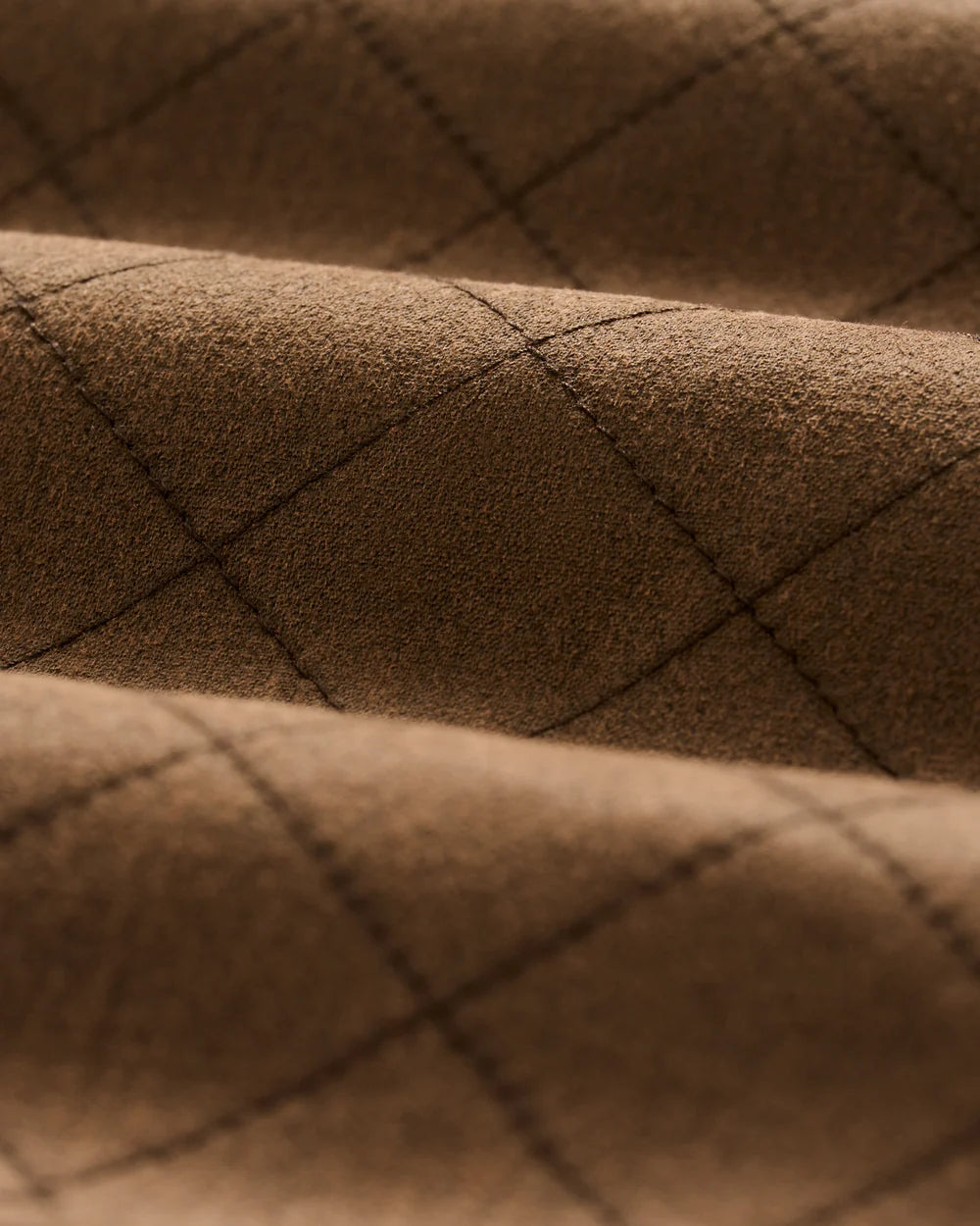Close-up of a brown textured fabric with a diamond quilted pattern stitched in a darker brown thread.